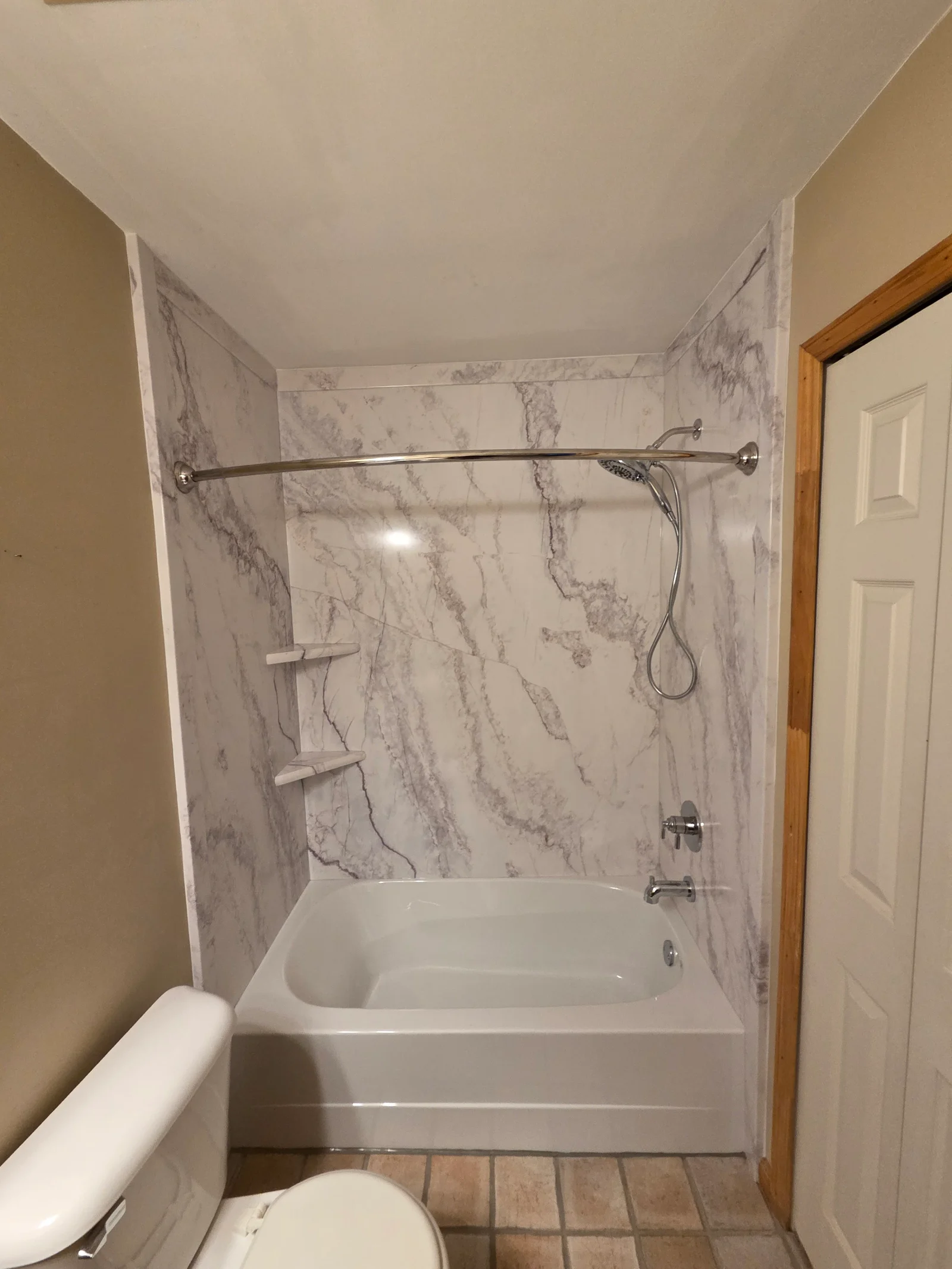 Bathroom tub with white marble-look wall panels, chrome curved shower rod, handheld shower, and built-in shelves