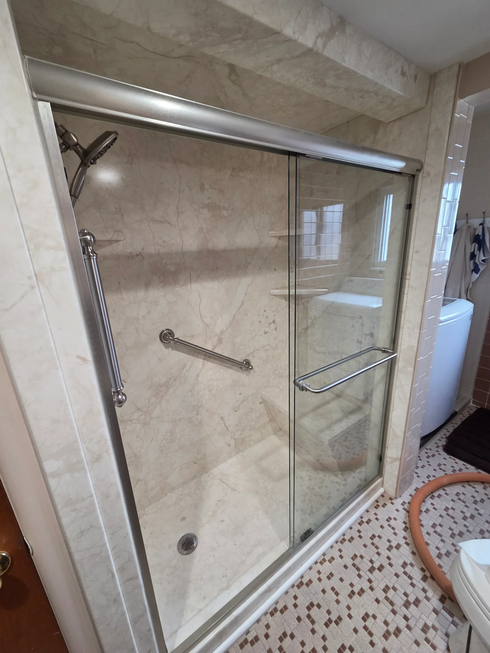 Cream marble-look shower with brushed nickel sliding glass door, handheld showerhead, and chrome grab bar