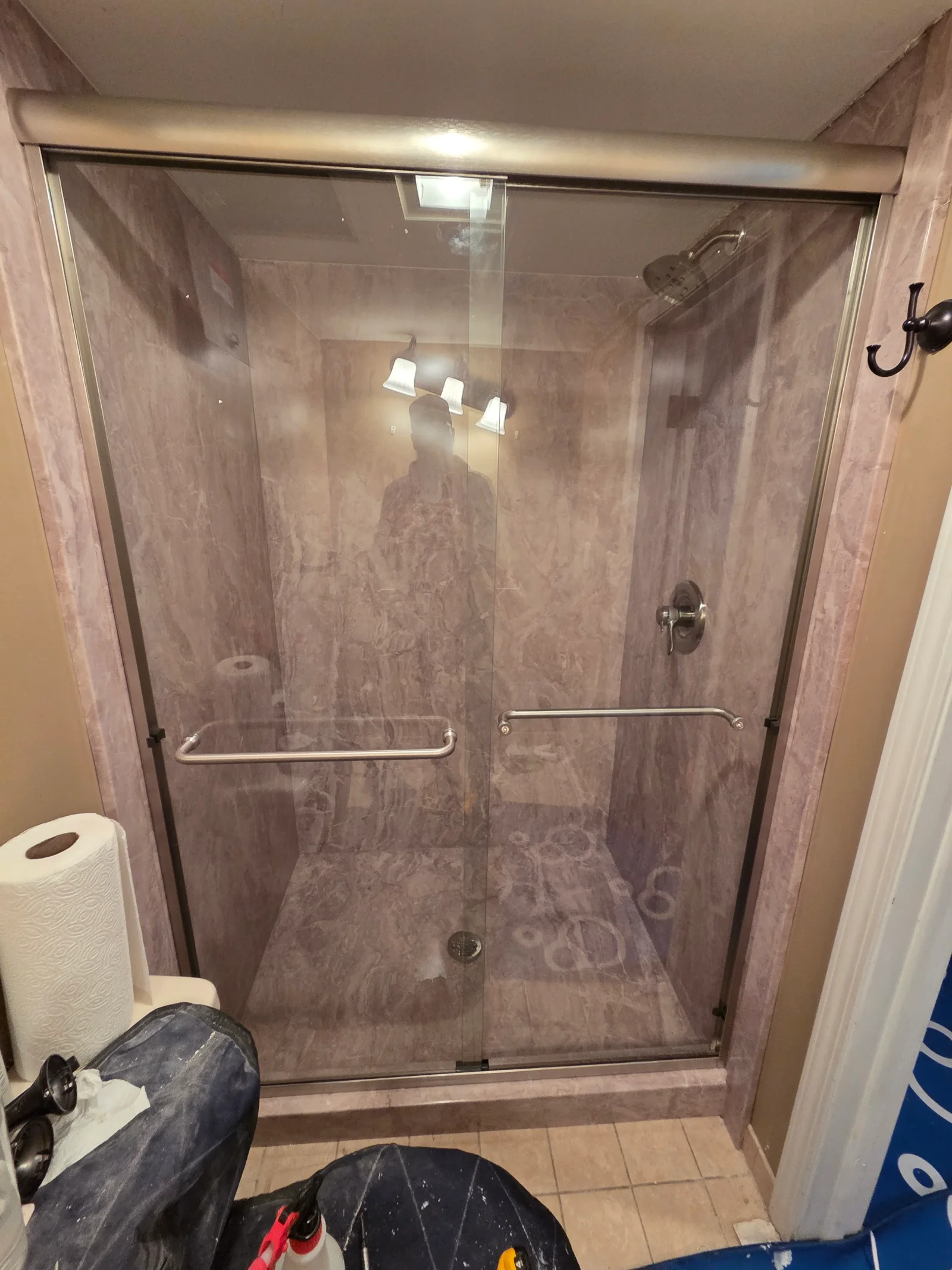 Shower with marbled pink wall panels, clear sliding glass door, brushed nickel frame and grab bars, and brushed nickel showerhead